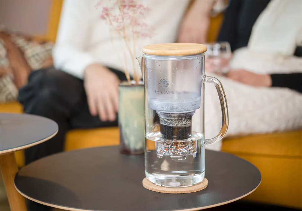 Three friends share a happy moment at an outdoor table, with the Lotus Vita ENYA glass water filter pitcher and a glass of fresh water.
